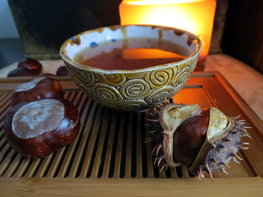 Roasted chestnuts and tea in ceramic bowl with candle