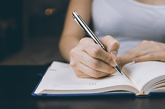 Close-up of woman writing in notebook with pen
