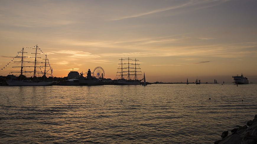 Silhouetted Tall Ships and Ferris Wheel at Sunset Harbor