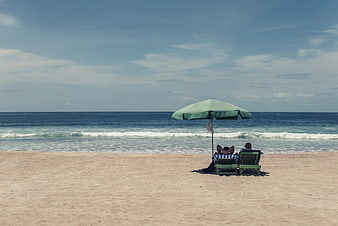 Couple Relaxing on Beach Lounge Chairs Under Green Umbrella