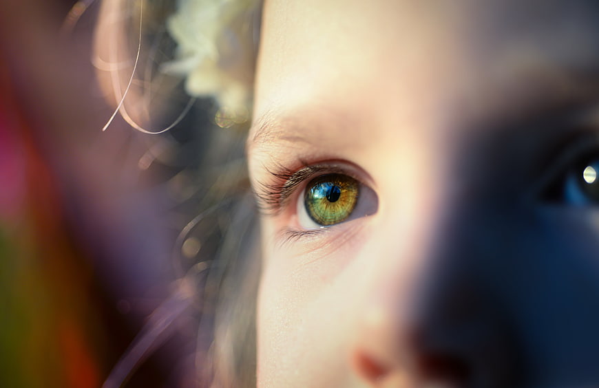 Close-up portrait of a girl's green eye with bokeh background