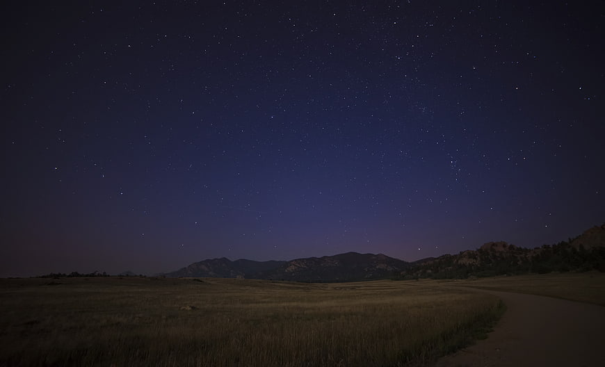 Starry Night Sky Over Grassy Field and Mountains