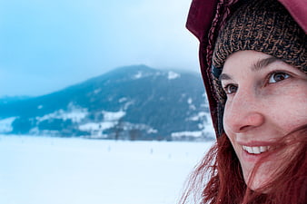 Close-up of smiling woman in winter hat with snowy mountain background