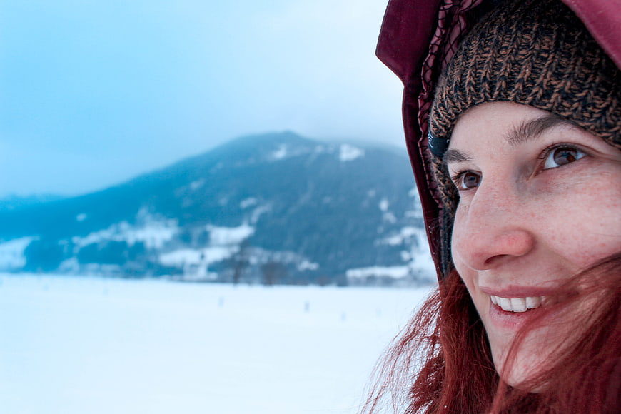 Close-up of smiling woman in winter hat with snowy mountain background