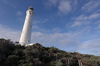 White stone lighthouse on coastal hill with blue sky