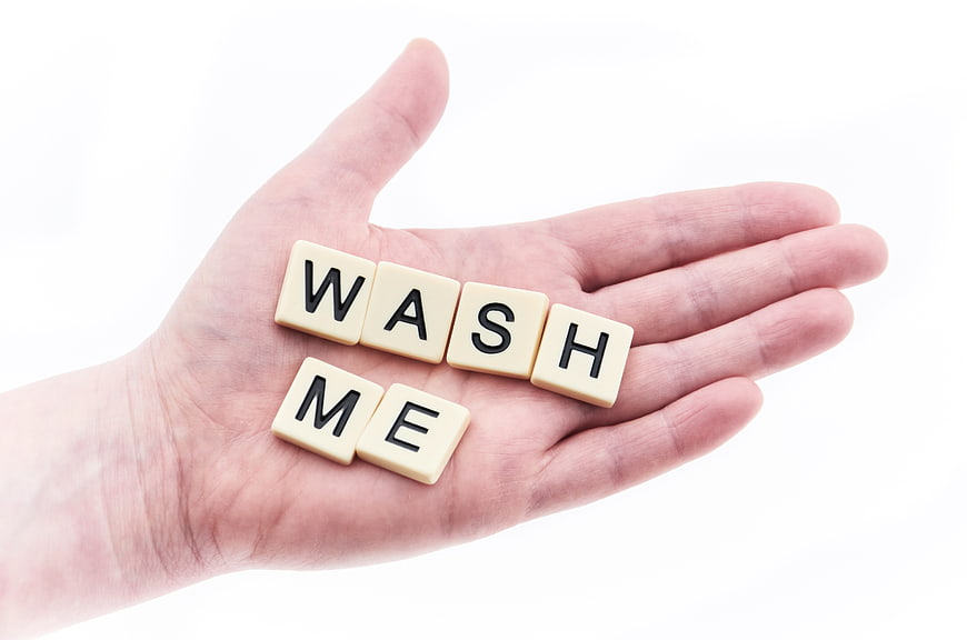 Hand holding Scrabble tiles spelling wash me on white background