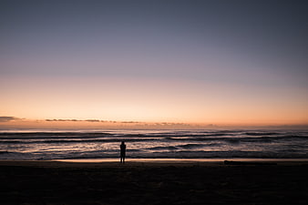 Silhouette of Person Standing on Beach at Sunset