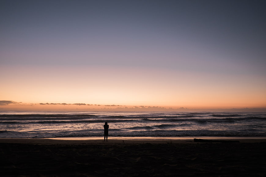 Silhouette of Person Standing on Beach at Sunset