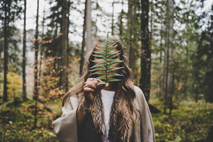 Woman holding fern leaf in autumn forest