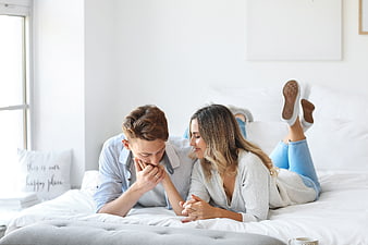 Happy young couple lying on white bed kissing hand