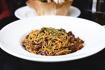 Close-up of beef noodles with sesame seeds in white bowl