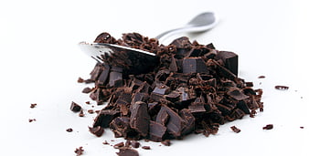 Pile of chopped dark chocolate pieces with spoon on white background
