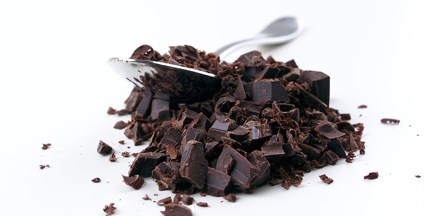 Pile of chopped dark chocolate pieces with spoon on white background