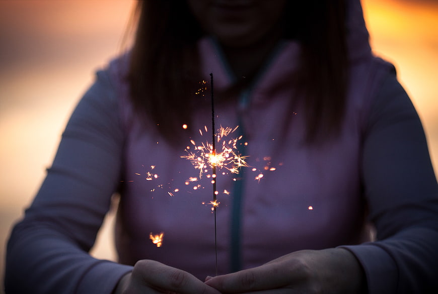 Woman holding sparkler at sunset