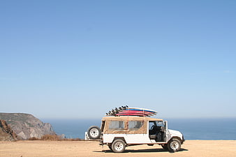 White SUV with surfboards parked on coastal cliff overlooking ocean