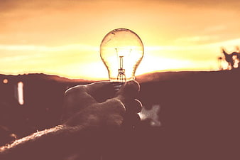 Hand Holding Light Bulb Against Golden Sunset Sky