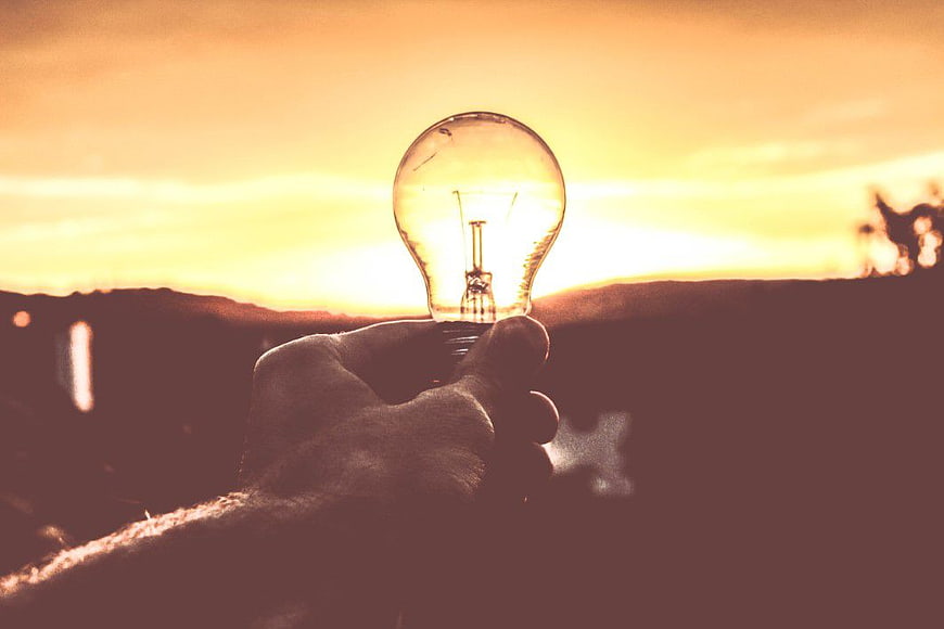 Hand Holding Light Bulb Against Golden Sunset Sky