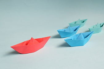 Red Origami Paper Boat Leading Blue Boats on Blue Background