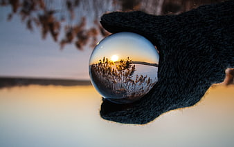 Hand holding crystal ball reflecting sunset landscape