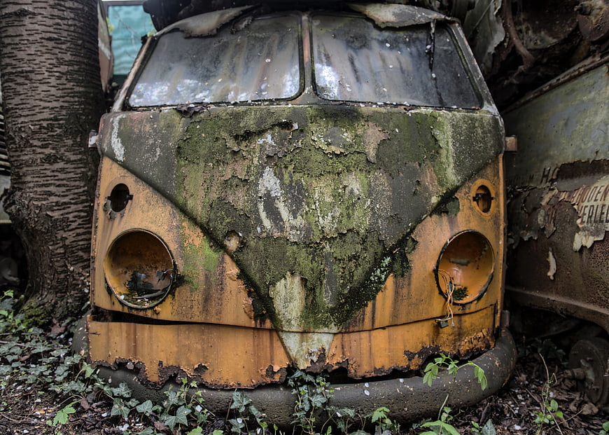 Rusty vintage VW bus front covered in moss and decay