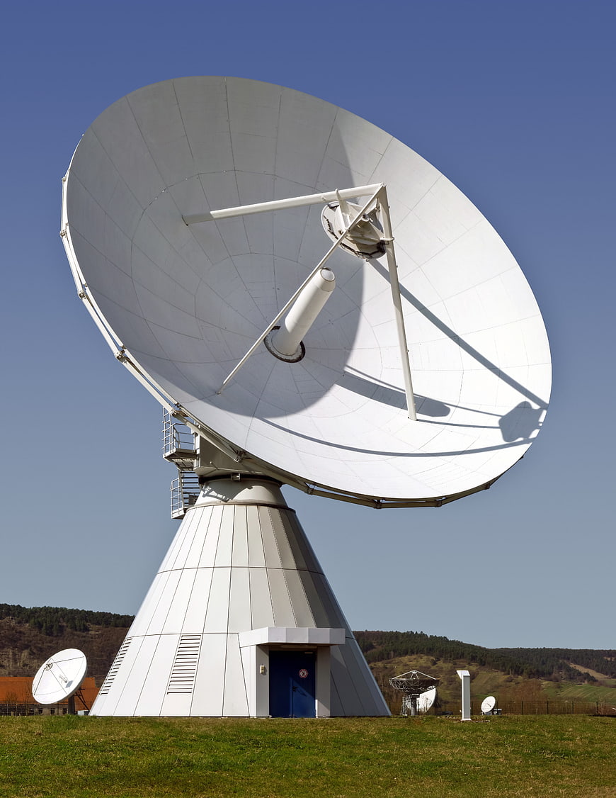 Large white satellite dish antenna on grassy hill
