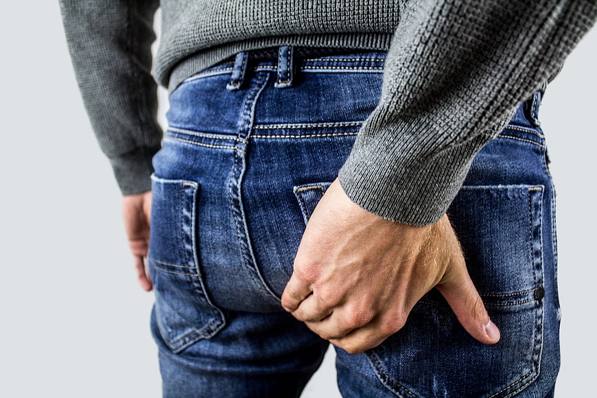 Man holding buttocks in pain wearing jeans and sweater