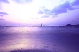 Dreamy purple long exposure bridge over calm ocean water