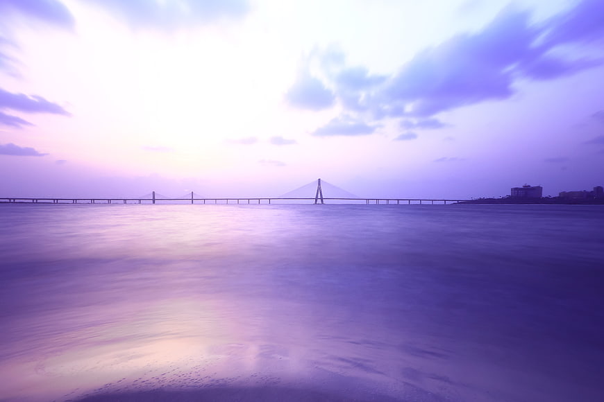 Dreamy purple long exposure bridge over calm ocean water