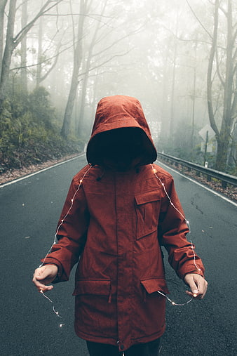Mysterious hooded figure with fairy lights on foggy forest road