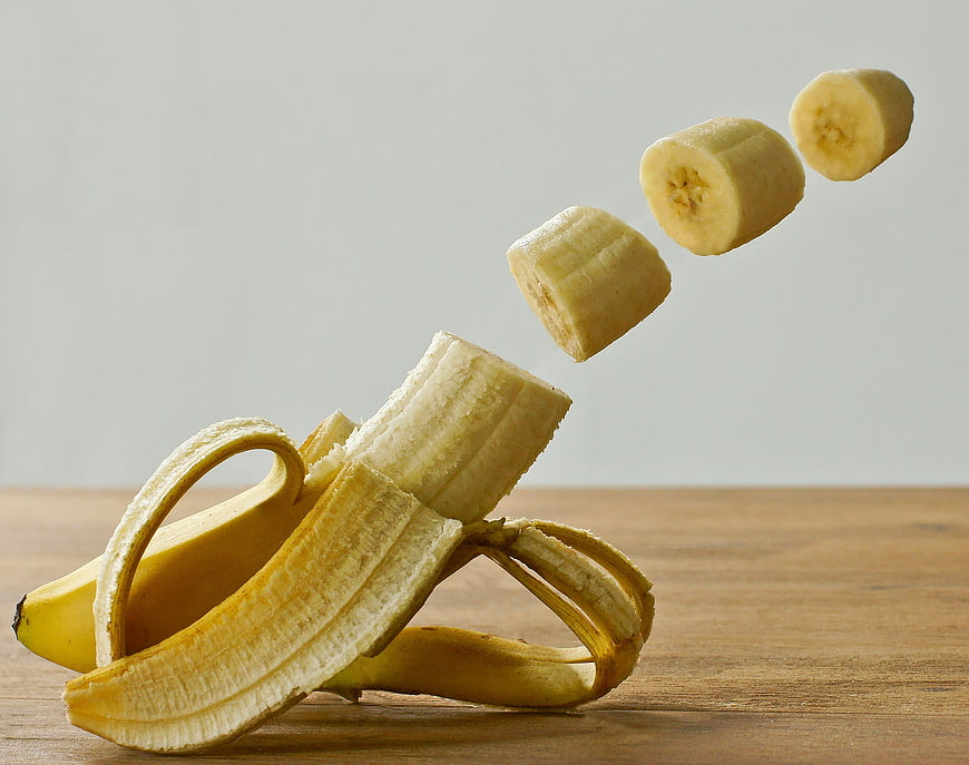 Flying banana slices emerging from peel on wooden table