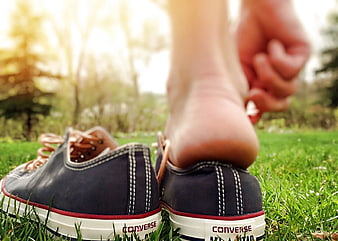 Close-up of bare feet stepping into black Converse sneakers on grass