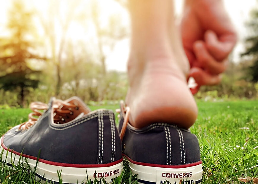 Close-up of bare feet stepping into black Converse sneakers on grass