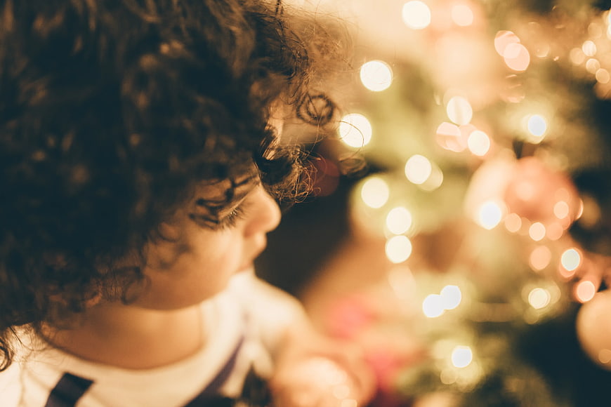 Child with curly hair looking at Christmas tree lights