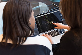 Two women collaborating on code at a laptop in an office