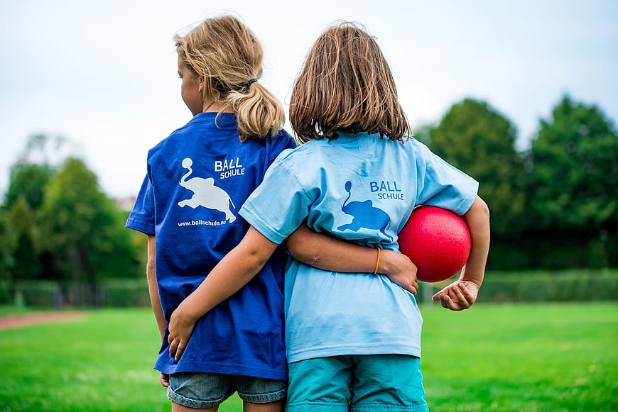 Two children in blue sports shirts standing together on a grassy field