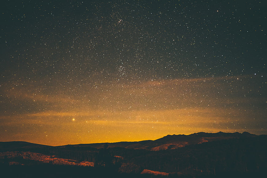 Starry Night Sky Over Mountain Landscape with Golden Horizon