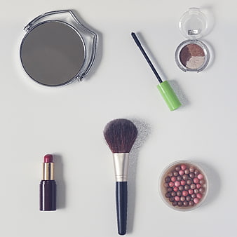 Flat lay of makeup tools, lipstick, and eyeshadow on white background