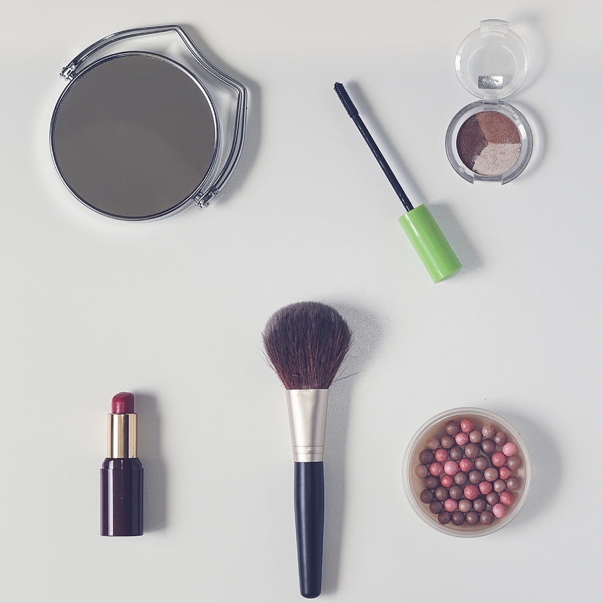 Flat lay of makeup tools, lipstick, and eyeshadow on white background