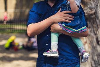 Father holding toddler girl in denim dress outdoors