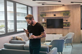 Smiling man with tattoos using smartphone in modern office lounge