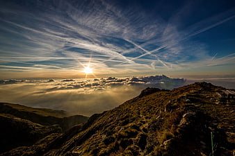 Sunrise over mountain ridge with sea of clouds and contrails