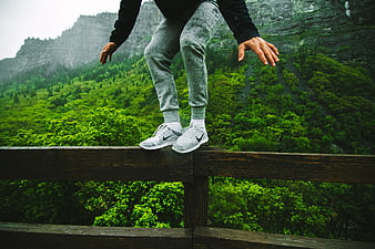 Person balancing on wooden railing with green mountain background