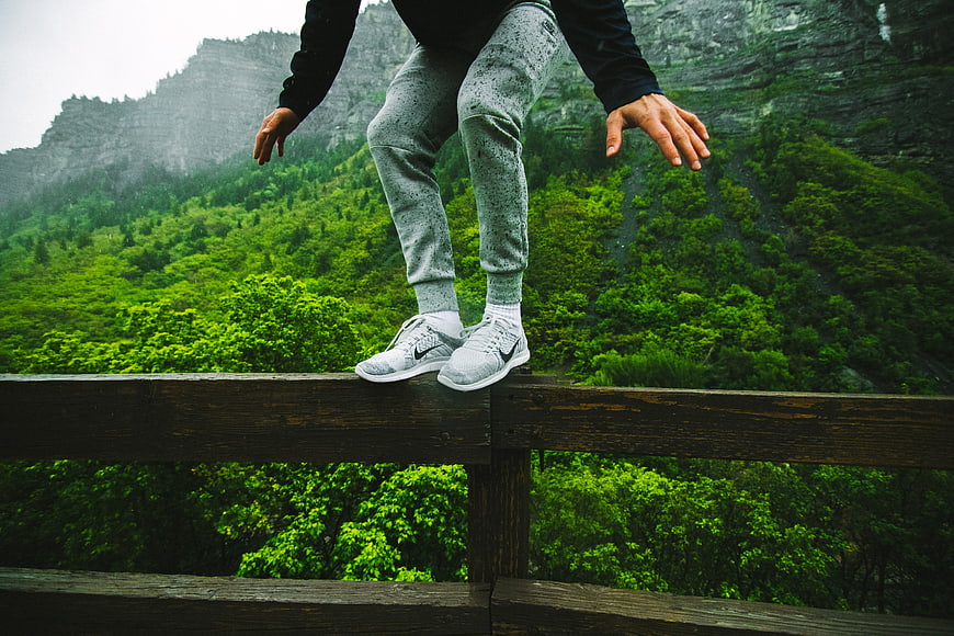 Person balancing on wooden railing with green mountain background