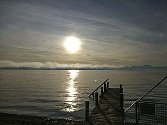 Sunrise over calm lake with wooden pier and distant mountains