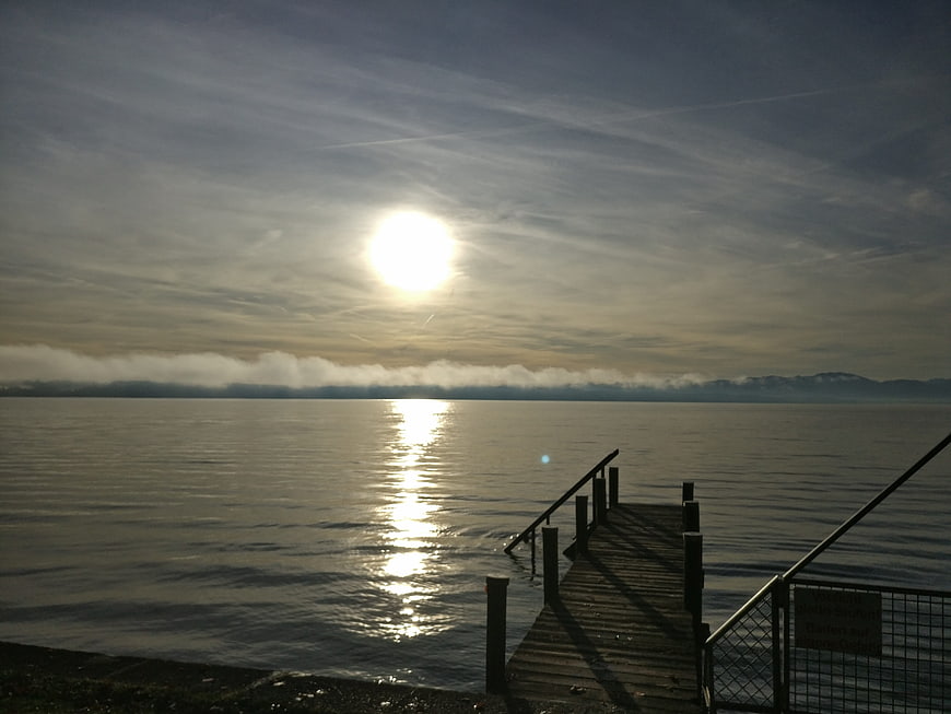 Sunrise over calm lake with wooden pier and distant mountains