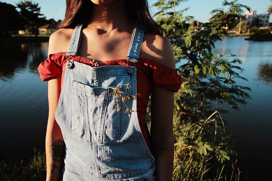 Woman in denim overalls and red top by lake