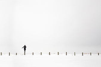 Woman walking in snowy winter landscape with wooden posts