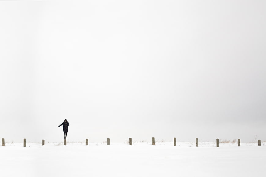 Woman walking in snowy winter landscape with wooden posts
