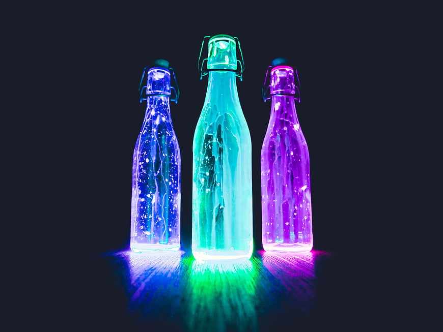 Three glowing glass bottles with neon liquid on dark background