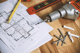 Construction blueprints and power drill on wooden workbench